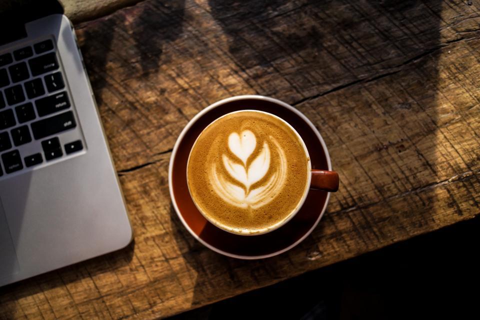 A cup of coffee next to a laptop on a wooden desk